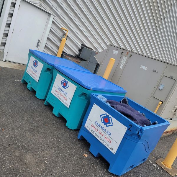 Three large blue bins are sitting in a parking lot.
